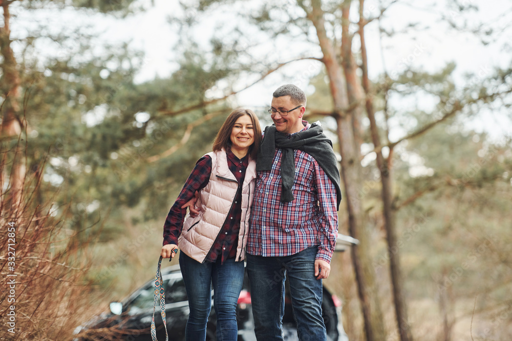 Fototapeta premium Happy mature couple have a walk in autumn or spring forest near modern car