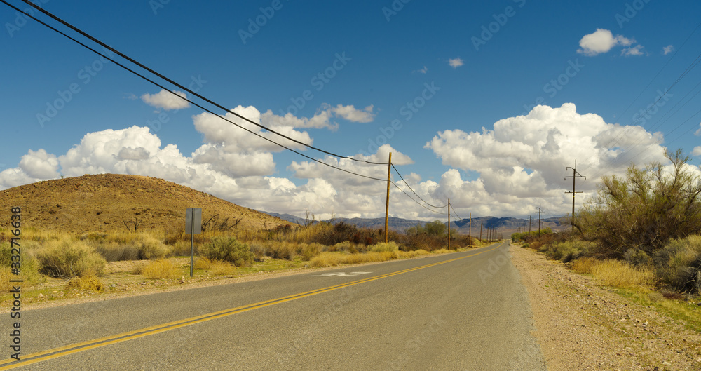 Old Spanish Trail Highway, looking east, near Tecopa in Inyo county. Image taken during a bright afternoon with white puffy clouds in the background.