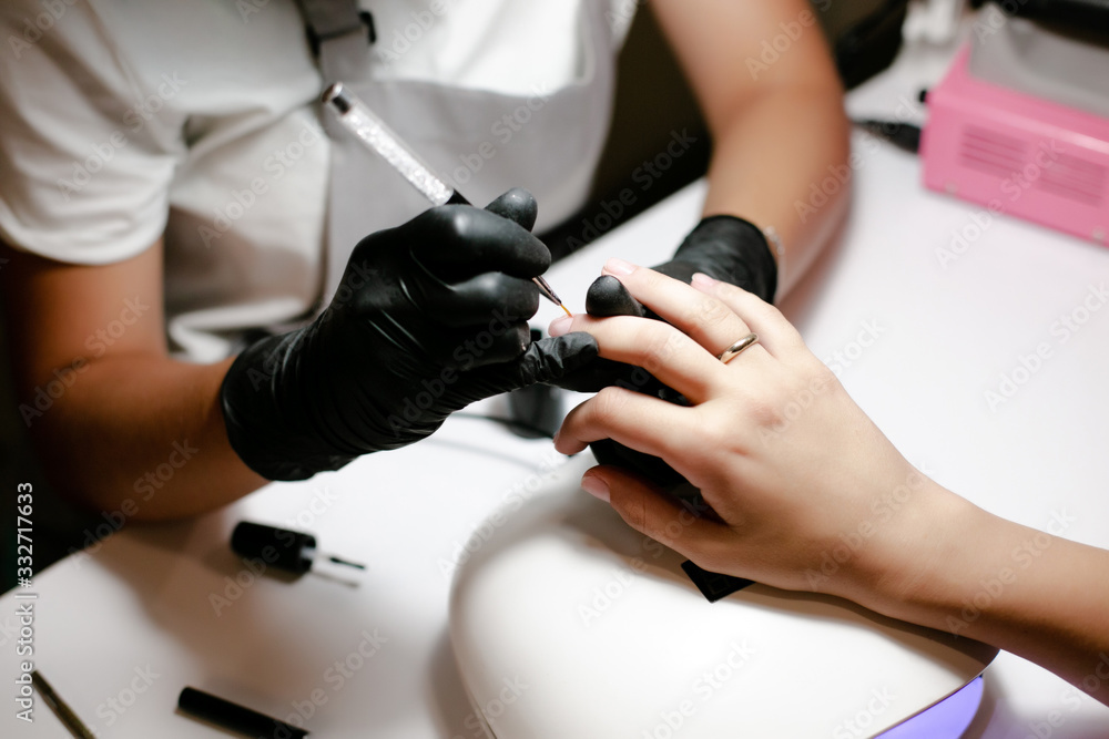 Close-up manicurist pushing cuticles on female nails with metal stick for cuticle in beauty salon.