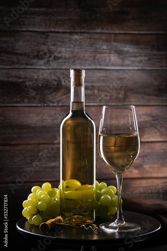 White full wine bottle and wineglass with grapes on a table on a wooden background