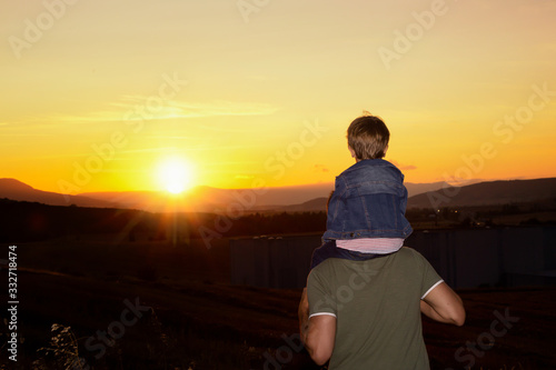 Boy climbed on his father s shoulders looking the sunset
