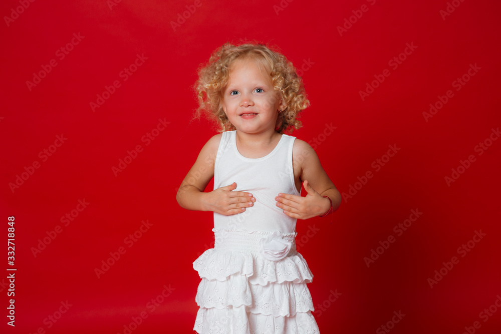 Pretty little blonde curly girl in white dress smiling isolated on red Pretty little blonde curly girl in white dress smiling isolated on red