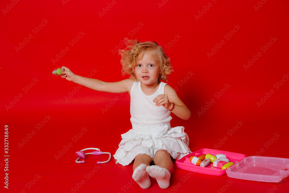 Adorable smiling little girl playing with toy syringe isolated on red. Child dream to be a doctor Adorable smiling little girl playing with toy syringe isolated on red. Child dream to be a doctor
