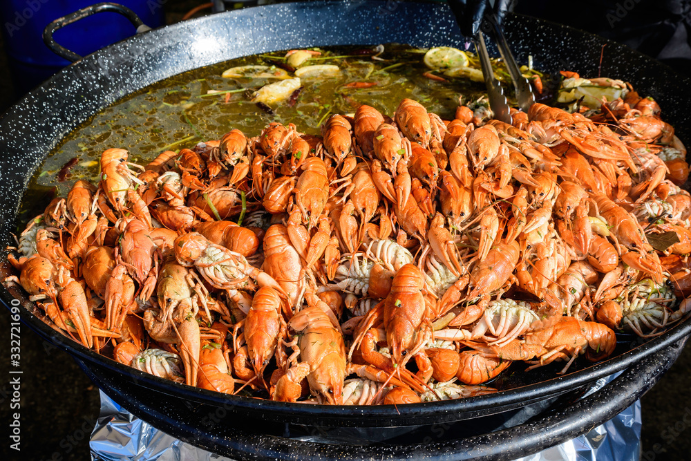 Close up of large portion of cooked shrimps with tomato sauce and yellow lemons in a large pan at a street food festival, ready to eat healthy seafood, beautiful orange monochrome outdoor background Close up of large portion of cooked shrimps with tomato sauce and yellow lemons in a large pan at a street food festival, ready to eat healthy seafood, beautiful orange monochrome outdoor background