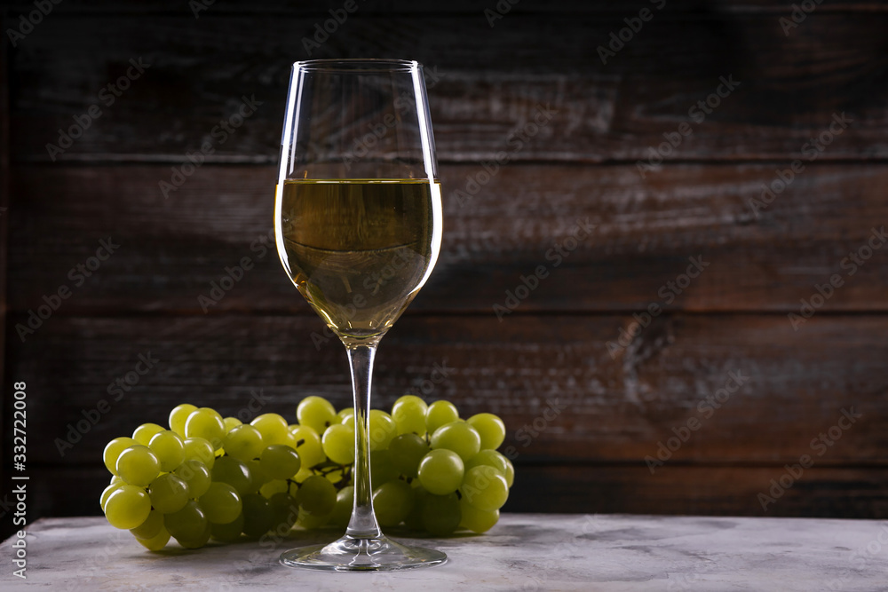 Fototapeta premium White wine glass with grapes on a table on a wooden background