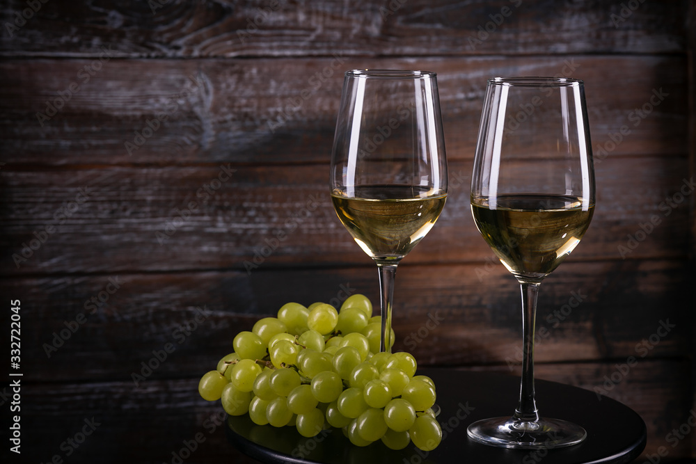 Two full white wine glasses with grapes on a table on a wooden background Two full white wine glasses with grapes on a table on a wooden background