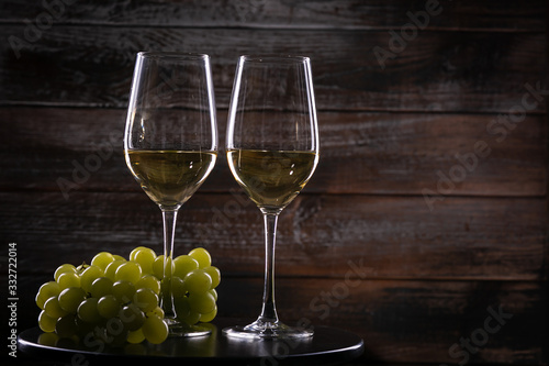 Two full white wine glasses with grapes on a table on a wooden background
