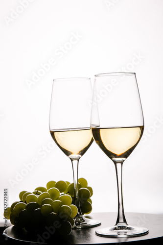 Two glasses with white wine and grapes on white background