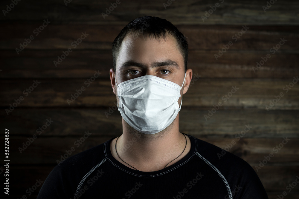 young man in medical mask on a dark wooden background young man in medical mask on a dark wooden background