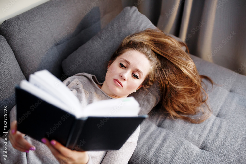 Smart young female relaxing at home, reading book on the couch Smart young female relaxing at home, reading book on the couch
