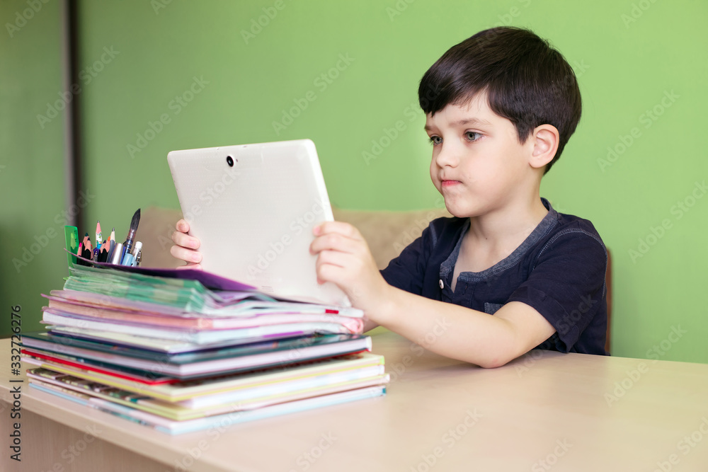 Boy using the tablet while doing homework during the coronavirus quarantine. Remote education concept. Boy using the tablet while doing homework during the coronavirus quarantine. Remote education concept.