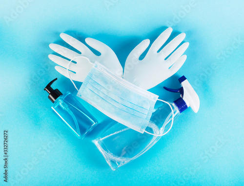 Medical mask, disinfection liquid, soap, latex gloves on blue background. Coronavirus protection concept in heart shaped composition. Protect yourself and prepare for the coronavirus