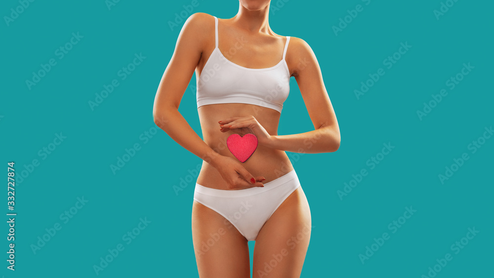 Obraz premium Fit young woman holding a heart over her abdomen, isolated on white background