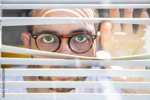 Young man with glasses looking through a blind Isolated