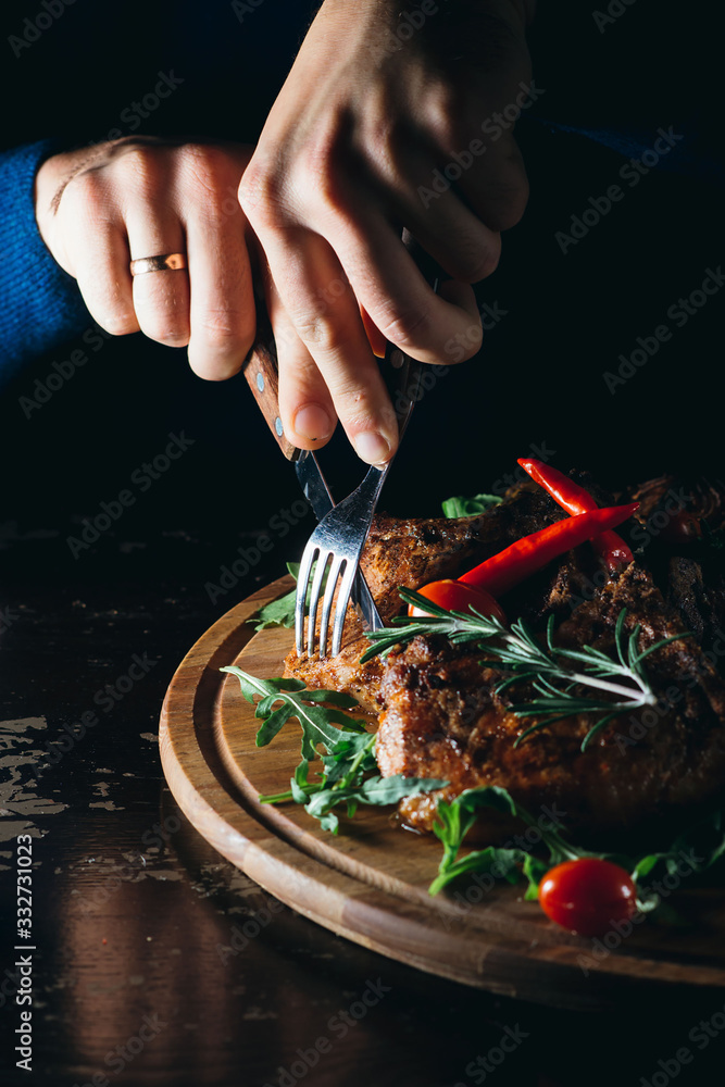 Man's hands cutting beef steak on a wooden plate with fork and a knife. Man is having a nice meal.