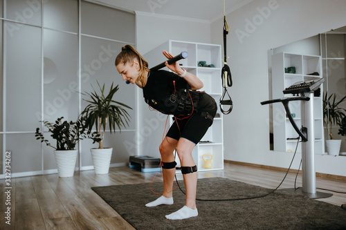 EMS training. Photo of young woman doing squats with a barbell in suit with cables.