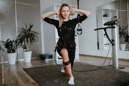 EMS training. Front view of young woman doing front lunges in suit with cables.