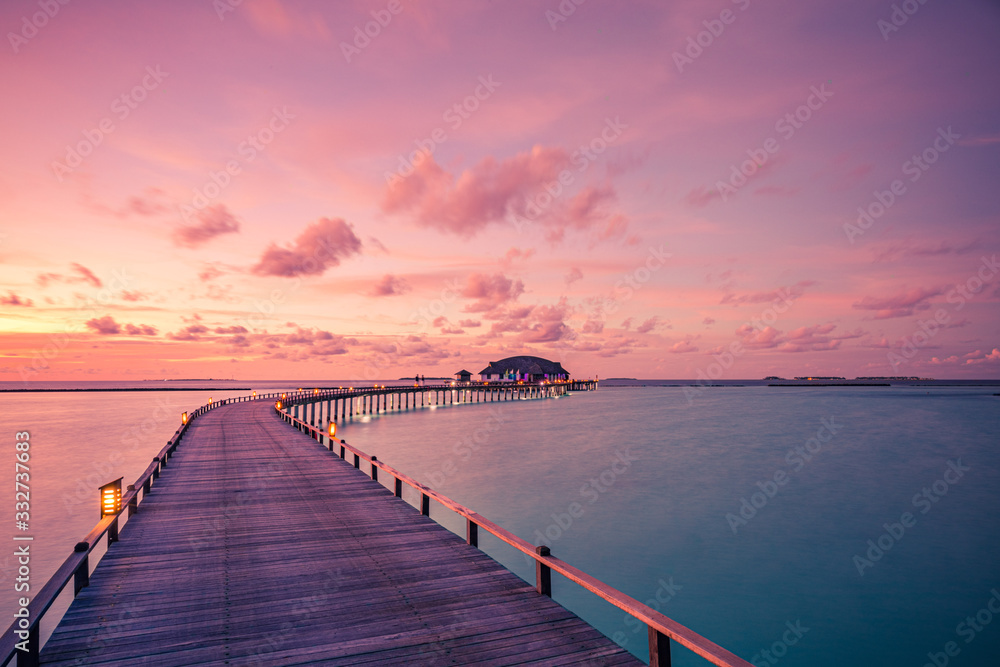 Sunset on Maldives island, luxury water bungalows villas resort and wooden pier. Beautiful sky and clouds and beach with seascape for summer vacation holiday and travel concept