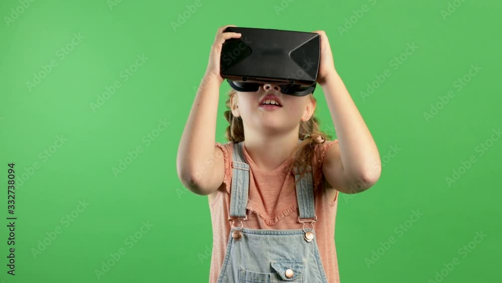 Slow motion smiling little girl having fun using VR glasses, girl standing on isolated green background. Concept of innovation, technology, family fun, games, next generation Slow motion smiling little girl having fun using VR glasses, girl standing on isolated green background. Concept of innovation, technology, family fun, games, next generation