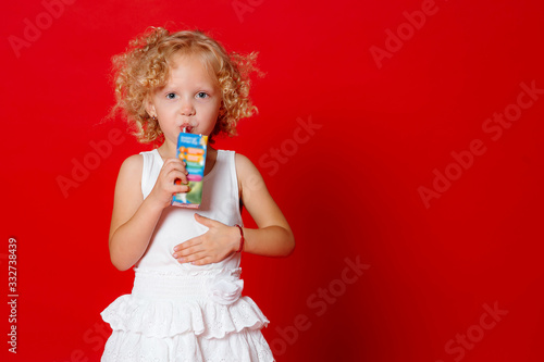 Cute curly girl in white dress drinking tasty juice isolated on red background © ChesterAlive91