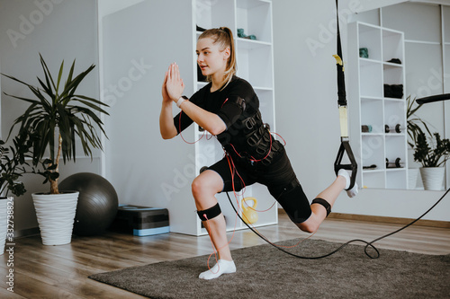 Konstfotografi Woman doing lunges in EMS electro stimulation suit with cables, using TRX