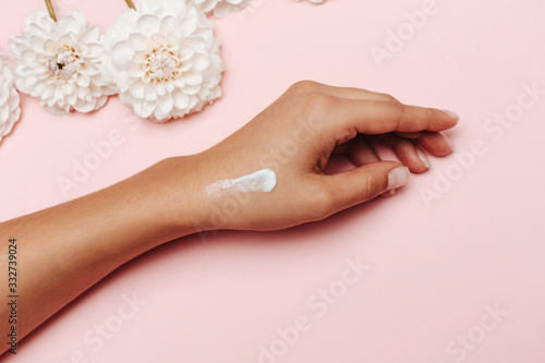 Woman's hand with white hand cream and dahlia flowers on pink background. The concept of self love.