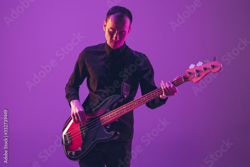 Photography Young and joyful caucasian musician playing guitar on gradient purple studio background in neon light