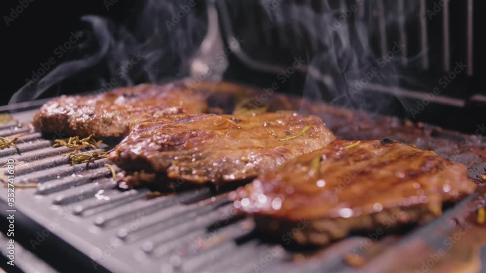 Delicious juicy meat steak cooking on grill. Aged prime rare roast grilling tenderloin fresh marble tenderness beef. Prime beef fry on electric roaster, rosemary, black pepper, salt. Slow motion. Delicious juicy meat steak cooking on grill. Aged prime rare roast grilling tenderloin fresh marble tenderness beef. Prime beef fry on electric roaster, rosemary, black pepper, salt. Slow motion.
