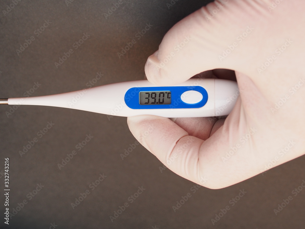 Obraz premium The electronic thermometer is held by a hand in a medical rubber glove. The display shows 39 degrees Celsius.