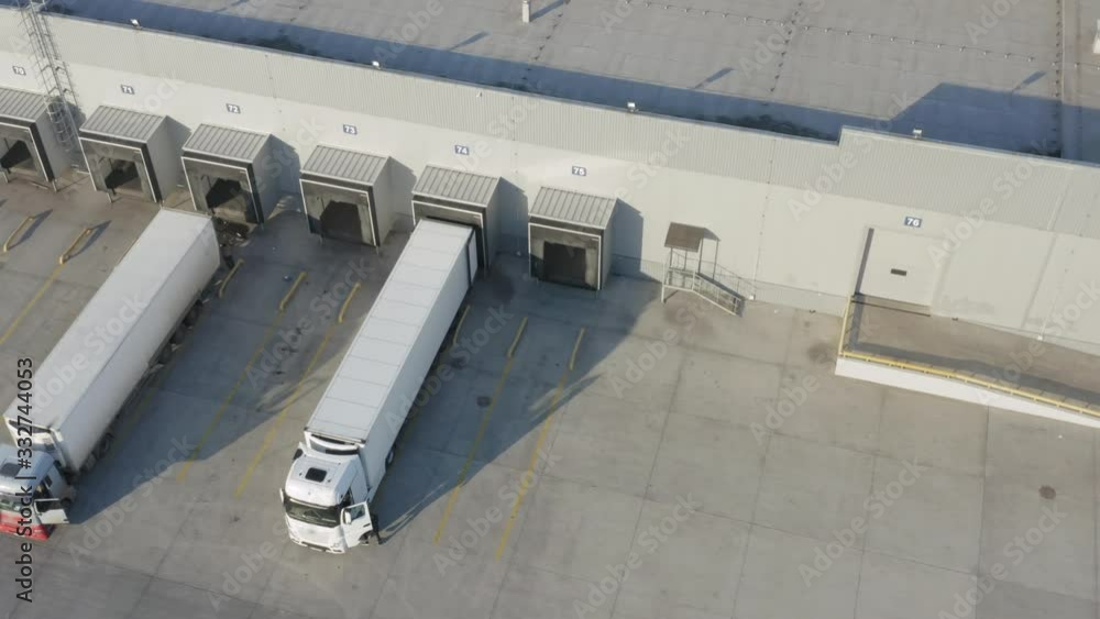 Aerial view of the logistics park with warehouse and semi trucks with cargo trailers standing at the ramps for load/unload goods Aerial view of the logistics park with warehouse and semi trucks with cargo trailers standing at the ramps for load/unload goods
