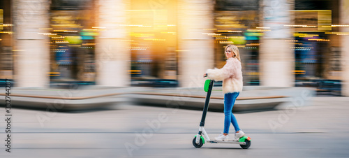 Young woman girl riding electric scooter downtown in city street urban