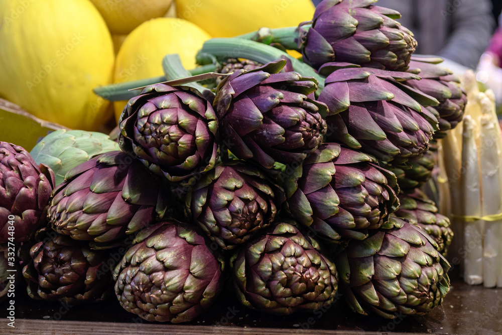 Obraz premium Fresh ripe red purple organic globe artichokes displayed for sale at a street food market, side view of healthy vegan food photogrpahed with soft focus