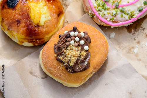 One large freshly deep fried donut coated with chocolate and colored candies, on a brown paper, in display for sale at a street food market, selective focus