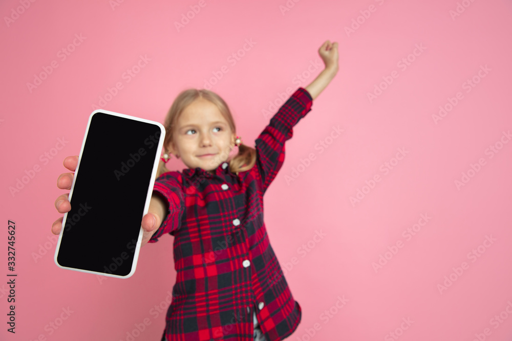 Showing blank screen. Caucasian little girl's portrait on pink studio background. Beautiful female model with blonde hair. Concept of human emotions, facial expression, sales, ad, youth, childhood. Showing blank screen. Caucasian little girl's portrait on pink studio background. Beautiful female model with blonde hair. Concept of human emotions, facial expression, sales, ad, youth, childhood.