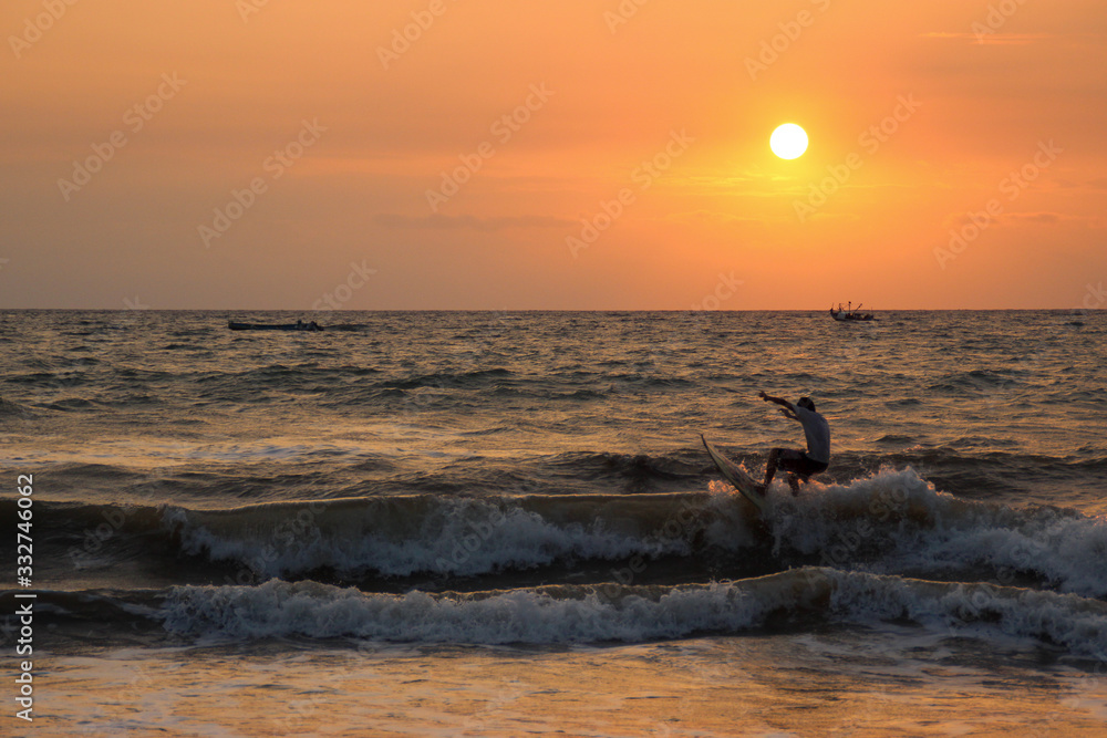 silhouette of a boy surfing at sunset