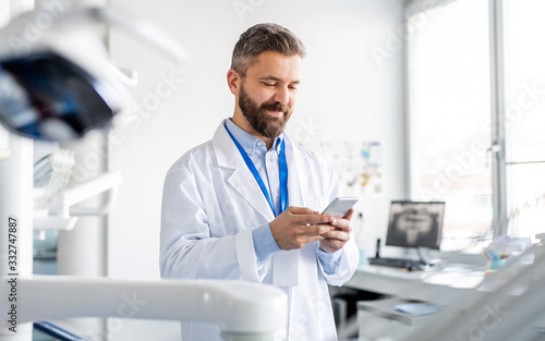 Dentist in modern dental surgery, using smartphone.