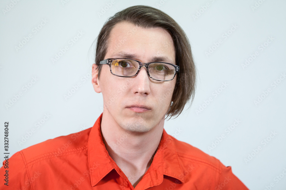 Calm and sanquine young Caucasian man with long hair and eyeglasses on face, looking at camera, grey background