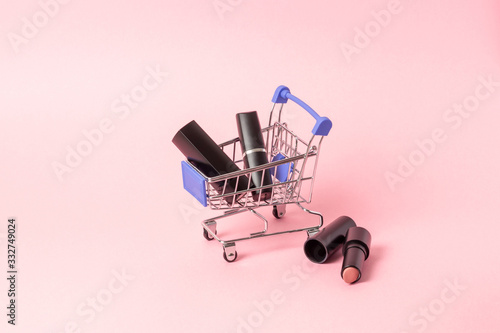 Lipsticks in black cases are located in a shopping trolley on a bright pink background. Cosmetics purchase concept, online shopping.