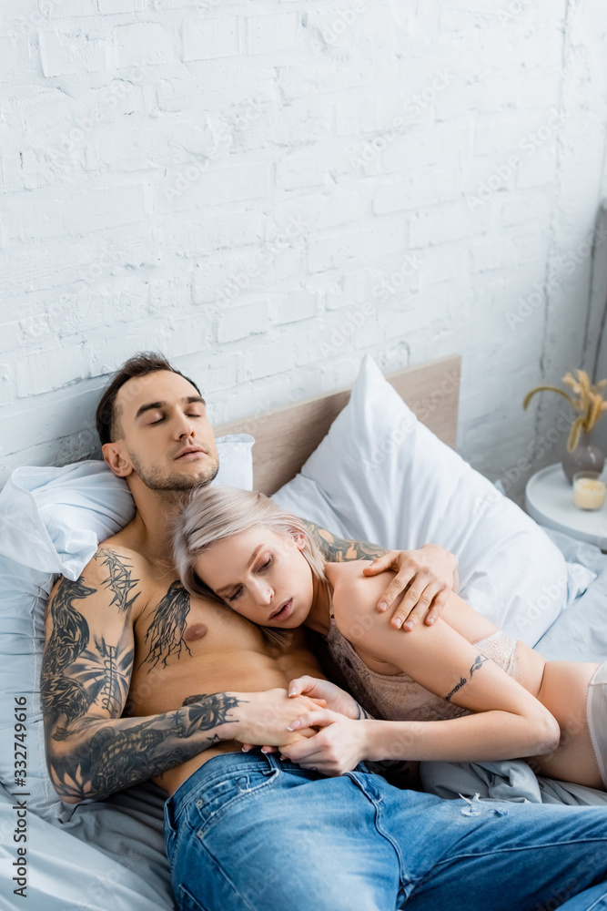 Attractive girl in underwear touching hand of muscular tattooed boyfriend on bed Attractive girl in underwear touching hand of muscular tattooed boyfriend on bed