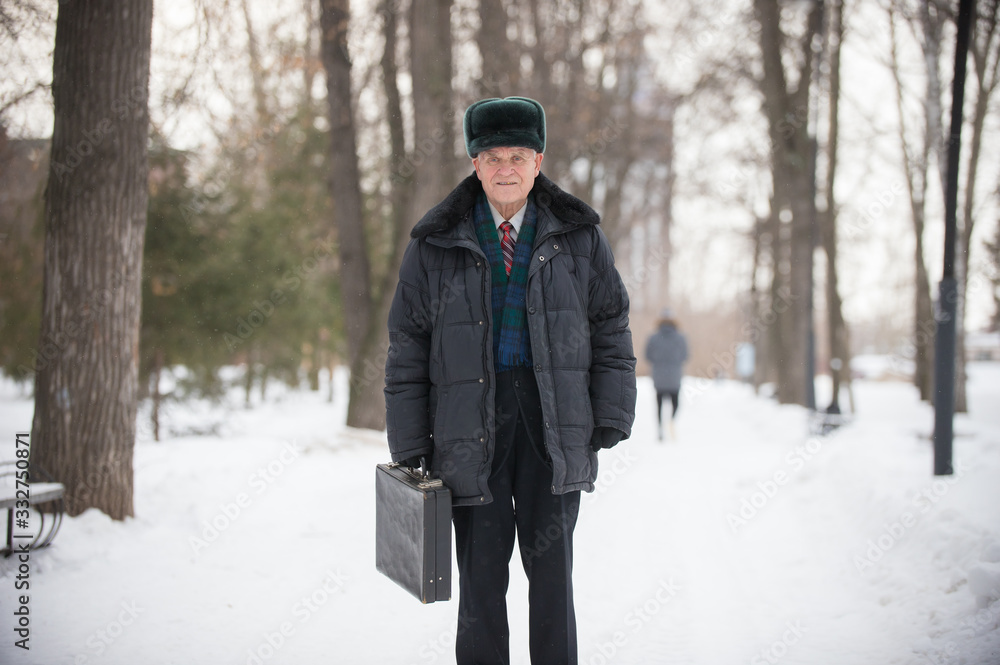 An old smiling man with case standing outdoors in winter park An old smiling man with case standing outdoors in winter park