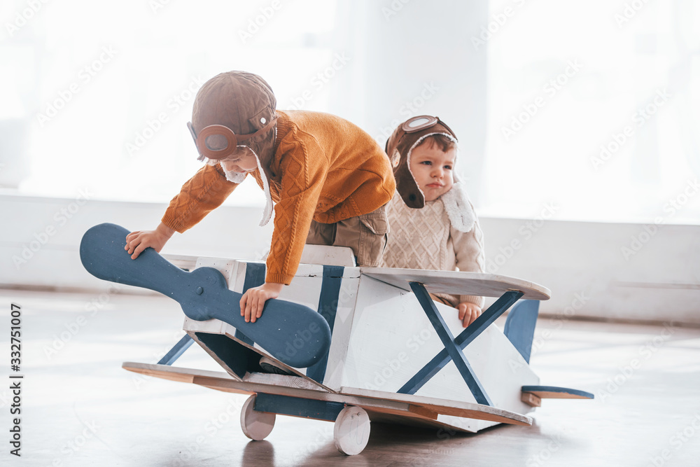 Obraz premium Two little boys in retro pilot uniform having fun with toy plane indoors