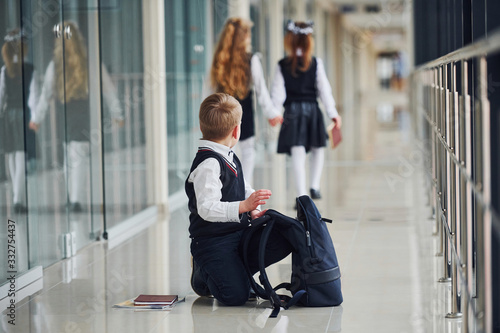 Boy sitting on the floor. School kids in uniform together in corridor