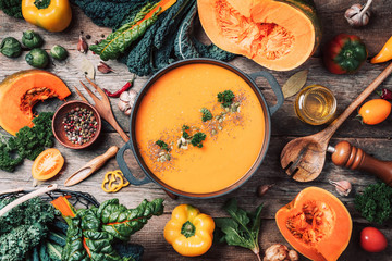 Pumpkin soup with vegetarian cooking ingredients, wooden spoons, kitchen utensils on wooden background. Top view. Vegan diet. Autumn harvest. Healthy, clean food and eating concept. Zero waste