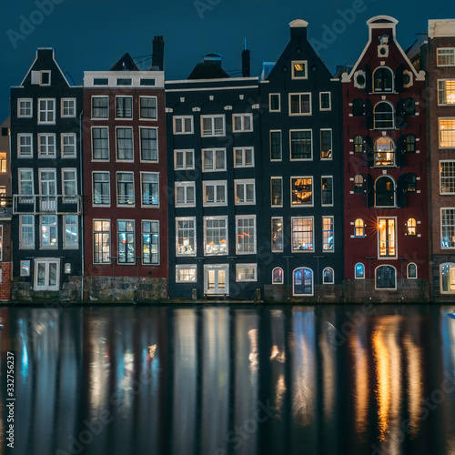 Famous dancing houses and buildings in Amsterdam with reflection in canal water at night, beautiful European landscape.