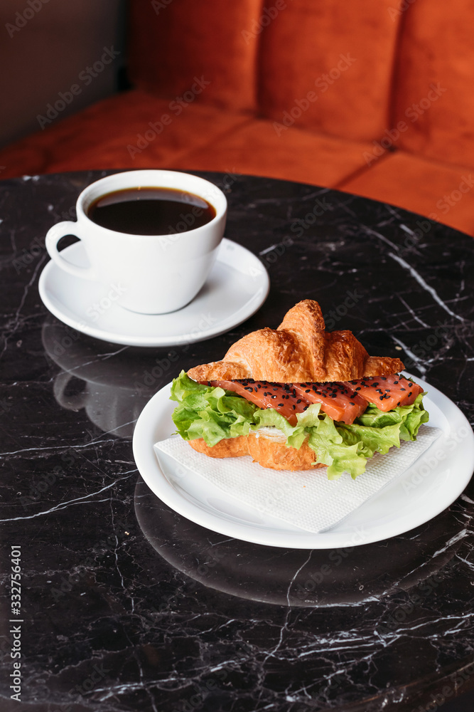 Croissant with salmon and herbs. Breakfast in cafe. Croissant with cup of black coffee. Croissant with salmon and herbs. Breakfast in cafe. Croissant with cup of black coffee.