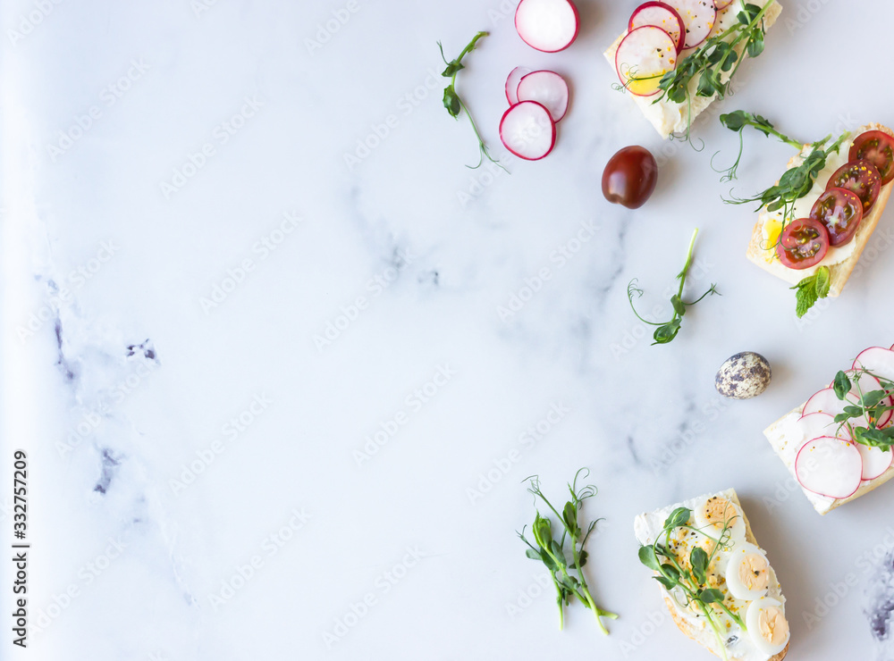 Variety of sandwiches with quail eggs, tomatoes, radish and micro green on a light grey background, selective focus. Party starter or appetizer. Flat lay composition.