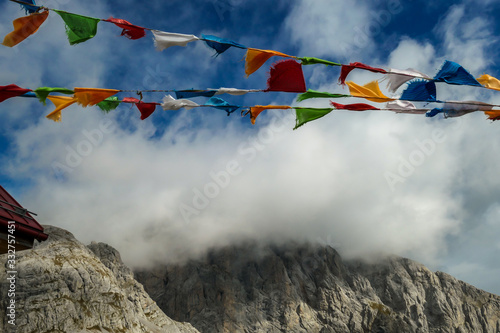 Prayer flags waving with the strong wind in Alpine mountain range at Austrian-Italian border. Sharp rocky Alpine peaks. Serenity and peace. Clouds breaching high mountains. Mantra and peace of mind