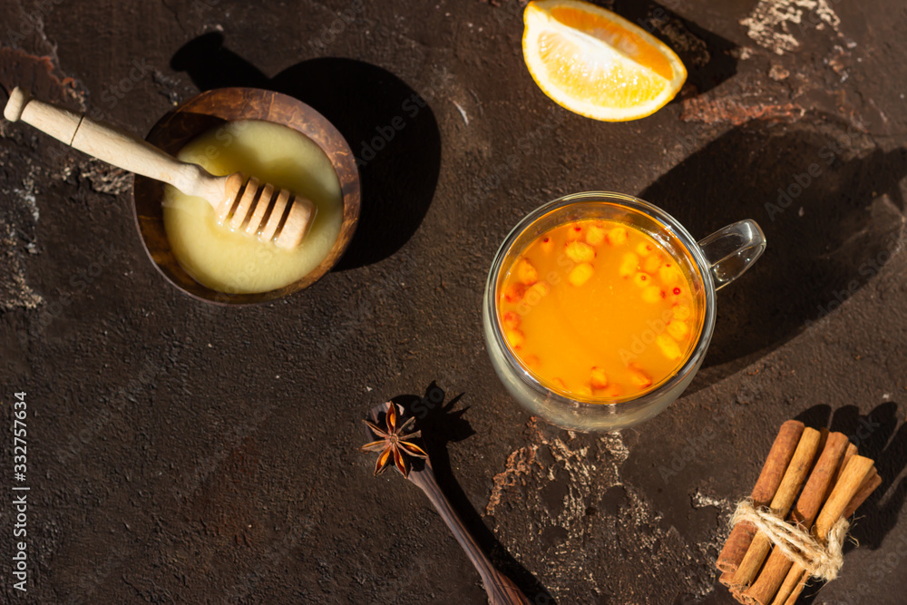 Φωτογραφία Colorful hot spicy sea buckthorn tea with cinnamon, anise and honey in glass cup on dark brown concrete background, selective focus