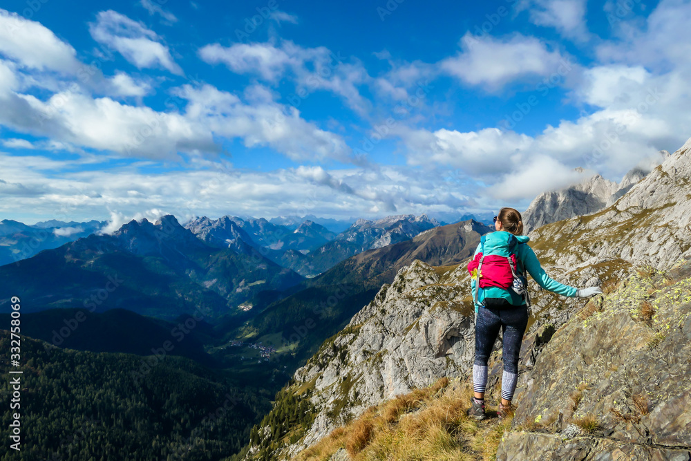 A woman reaching the top of Monte Coglians, Hohe Warte on the Austrian-Italian Alpine border. Very steep and narrow pathway that she walks on. She is not giving up, visible goal. Stunning view