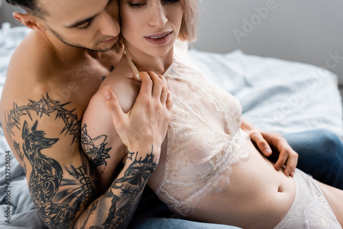 Cropped view of tattooed man embracing beautiful girl in underwear on bed